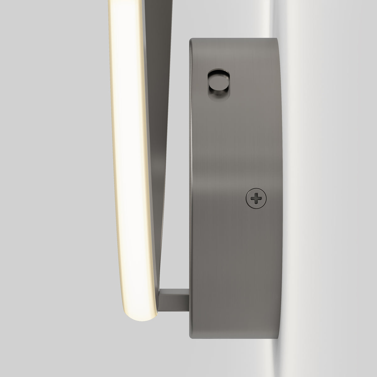A close-up side view of a modern wall-mounted light fixture with a curved, illuminated strip and a sleek, brushed metal base attached to a light gray wall.