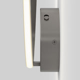 A close-up side view of a modern wall-mounted light fixture with a curved, illuminated strip and a sleek, brushed metal base attached to a light gray wall.