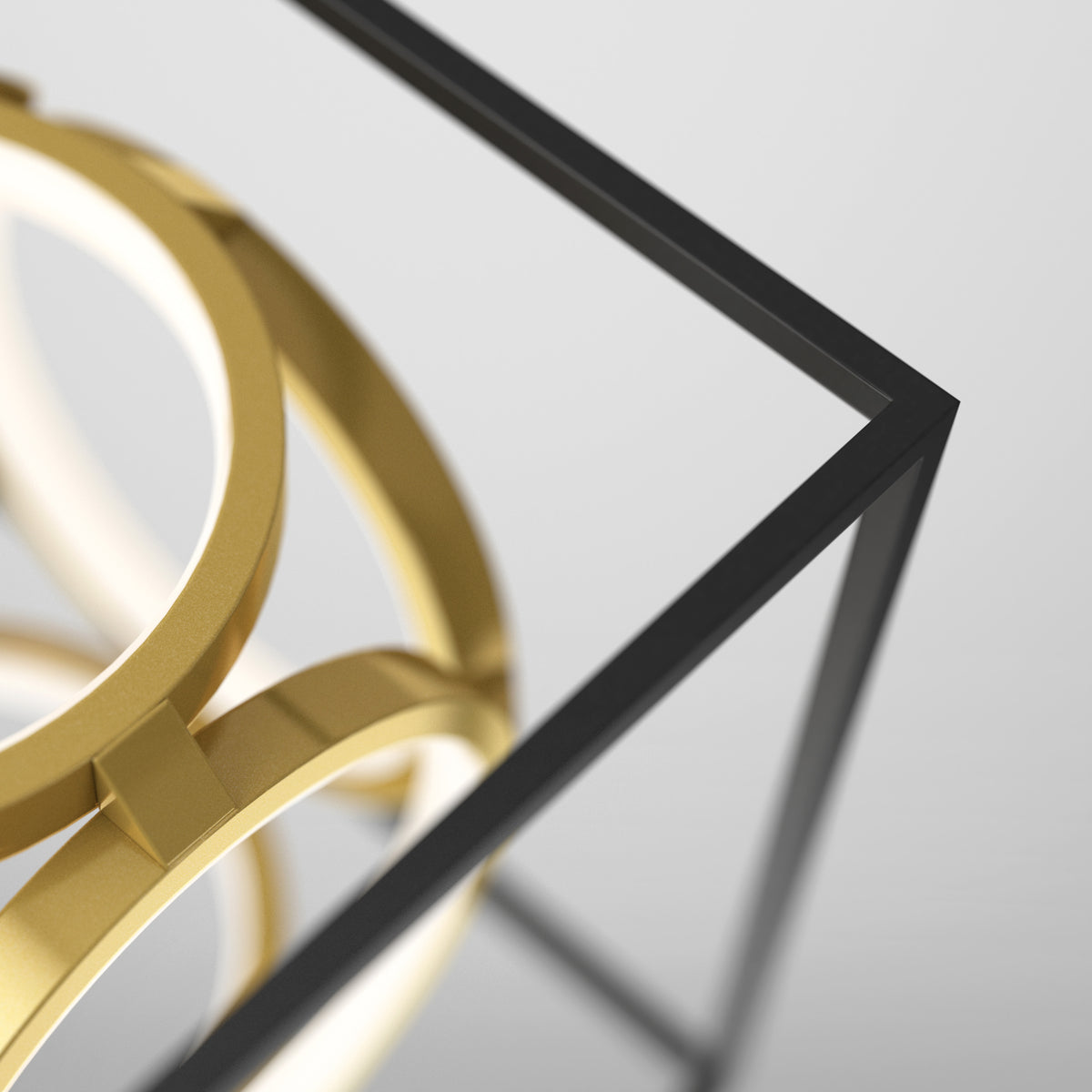 Close-up of a modern abstract sculpture featuring interlocking gold rings within a minimalistic black metal cube frame on a light background.