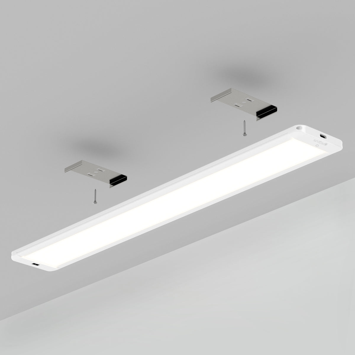 A white rectangular LED ceiling light fixture is shown mounted to a grey ceiling with two metal brackets and visible screws for installation. The light is turned on, emitting a bright glow.