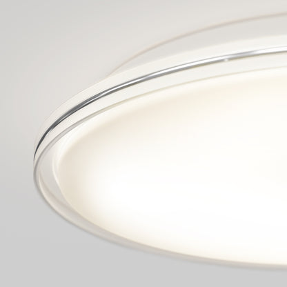 A close-up of the Artika Astrid 16.5 in. LED flush mount light with 5 CCT and remote, featuring a frosted white cover and sleek metallic rim, emits a soft, even glow against a light gray background.