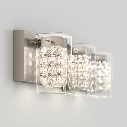 The Artika Crystal Cube LED bathroom vanity light 5 CCT features a brushed metal base and clear, textured glass shade, casting bright white light on a plain, light-colored wall.
