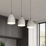 Three modern, cone-shaped pendant lights with a concrete finish hang from the ceiling in a minimalistic kitchen with dark cabinets and large windows.