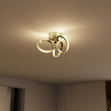 A modern ceiling light fixture with three intertwined, illuminated loops emits a warm glow, mounted on a beige ceiling in a contemporary room with minimal decor.