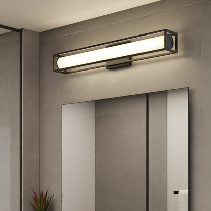 The Artika Venicia LED Wall Sconce, featuring a sleek black metal frame, is mounted above a large mirror on a gray bathroom wall. A plant and rolled towel are seen reflected in the glass.