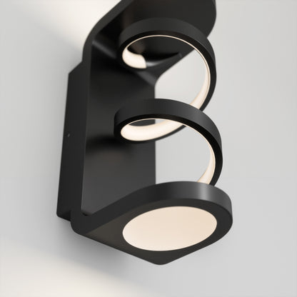The Artika Swirl indoor-outdoor LED wall light features two circular LED rings and a round base in a modern black design, offering clean lines and soft, diffused light—perfect for contemporary white walls.