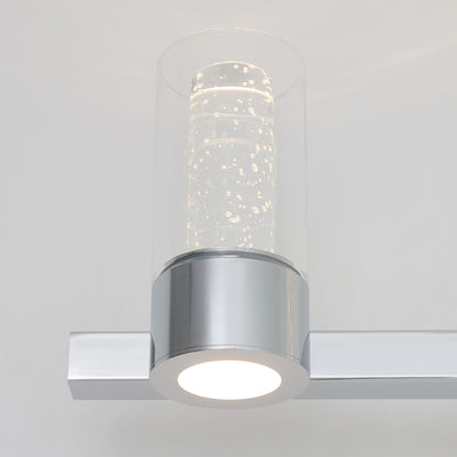 The Artika Novello modern LED bathroom vanity light features a chrome base and a cylindrical glass shade with bubble details, providing soft white illumination.