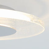 Close-up of a modern, circular ceiling light with a translucent edge embedded with small bubbles, emitting a soft, white glow against a light gray background.