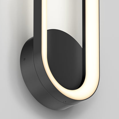 Close-up of the Artika Aiden modern LED indoor-outdoor wall light 5 CCT, featuring a black circular base and a smooth curved illuminated strip in a partial oval shape, mounted on a light-colored wall.