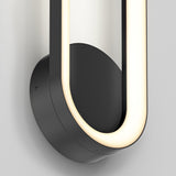 A modern wall-mounted light fixture with a circular black base and a U-shaped, glowing LED strip, set against a light gray background. The design is sleek and minimalist.