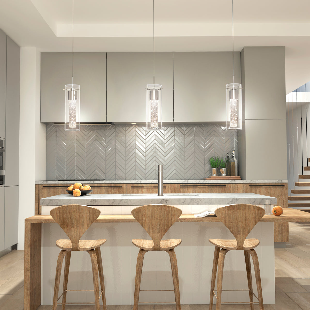 Modern kitchen with light gray cabinets, a herringbone tile backsplash, wooden island, three wooden bar stools, marble countertop, and three pendant lights. Some fruit and decorative greenery are on the counters.