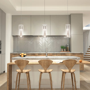 Modern kitchen with light wood and grey cabinets, a marble island with three wooden bar stools, Artikas Essence LED pendant lights above, a herringbone tile backsplash, fruit on the counters, and stairs in the background.