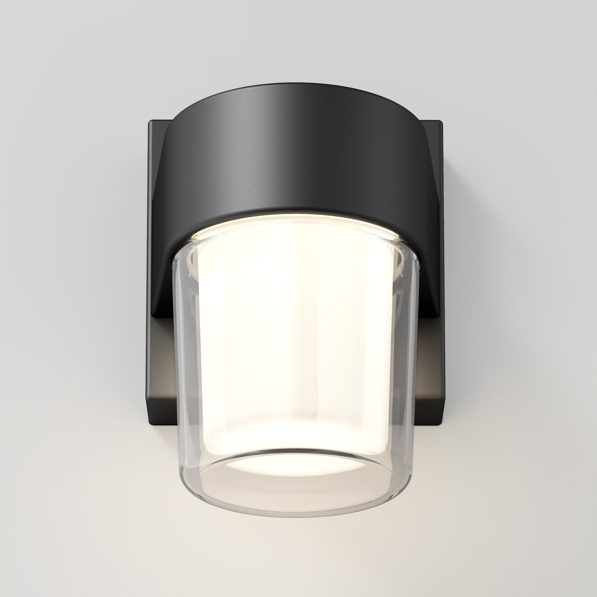 A modern wall-mounted light fixture with a matte black square base and a cylindrical frosted glass shade, emitting a soft, warm light against a plain white background.