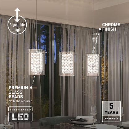 Three Crystal Cube 3-light LED pendant lights by Artika with chrome finish and glass beads hang over a table for two, in front of sheer curtains and a window with trees. Features include adjustable height, energy-efficient LEDs, and a 5-year warranty.