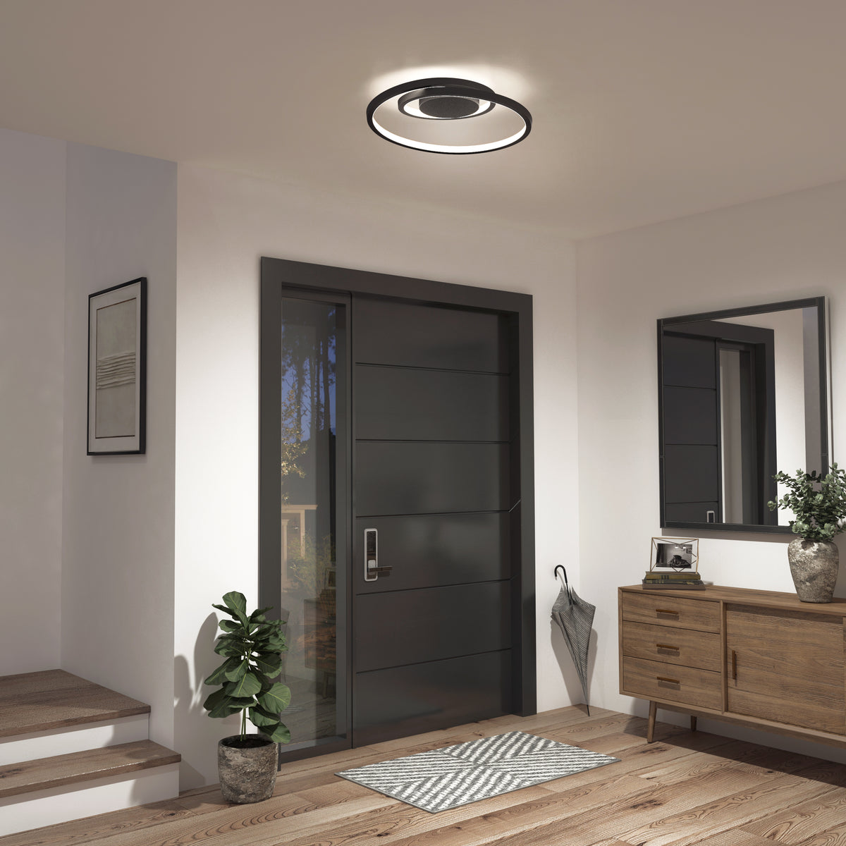 A modern entryway with a dark front door, round ceiling light, wooden sideboard with a mirror above, a small potted plant, a framed picture, and an umbrella tucked in the corner.