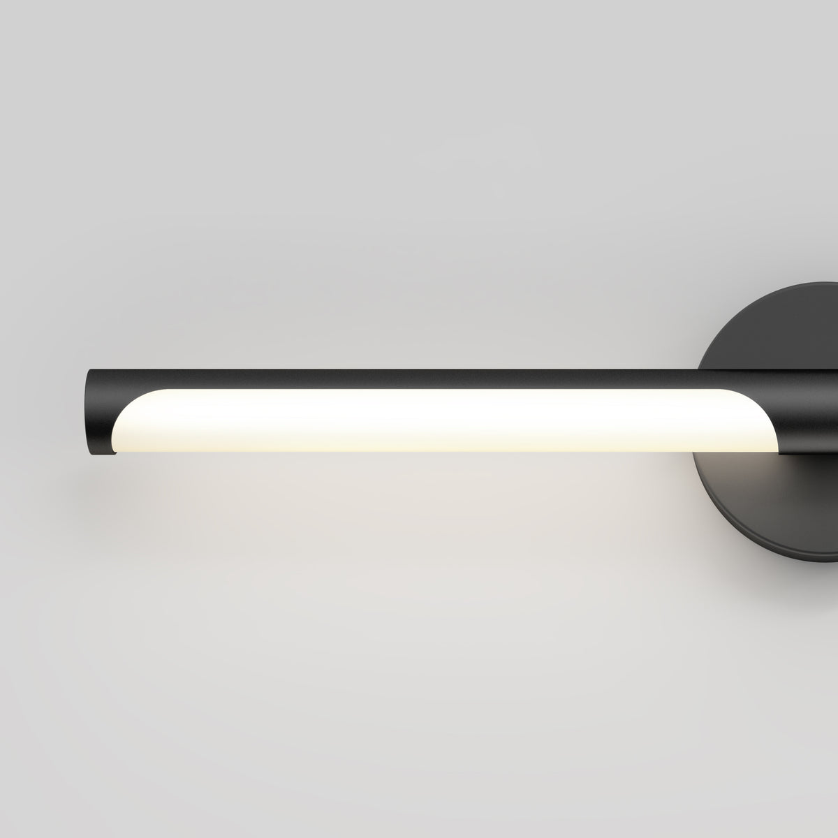A modern wall-mounted light fixture with a black cylindrical body, emitting soft white light, attached to a round black base against a plain light gray background.