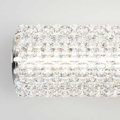 A close-up of the Artika Exalto LED bathroom vanity light, a cylindrical fixture decorated with sparkling crystals that emit bright white light, creating a shimmering effect against a plain light background.