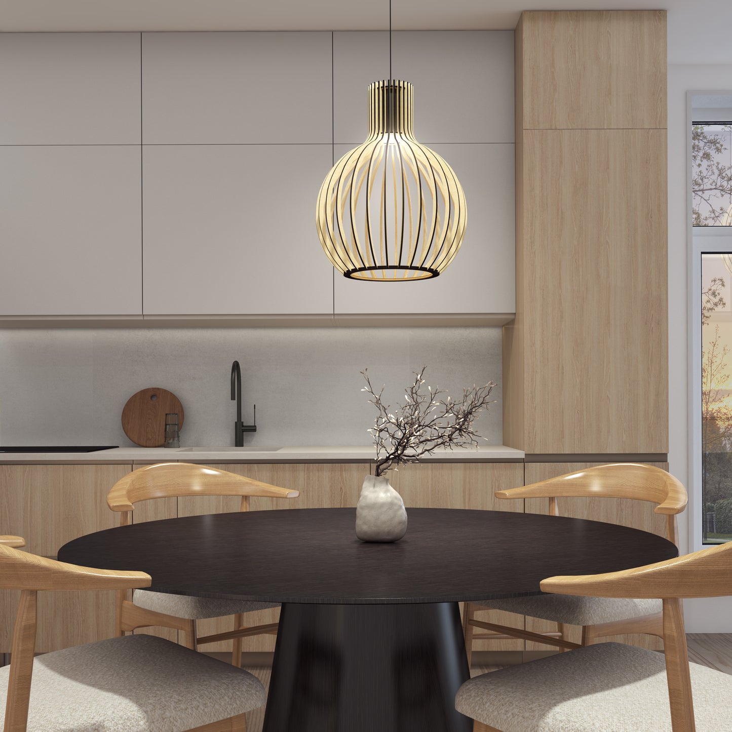 A modern kitchen with light wood cabinets, a round black table and four wooden chairs, a vase with branches, and the Artika Tomi LED Pendant Light 3 CCT stylishly hanging above. Sunlight streams in through a window on the right.