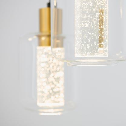 Close-up of two Champagne Globe 4-light LED pendants by Artika, featuring gold accents and cylindrical glass covers with illuminated bubble-like details inside, set against a light gray background.