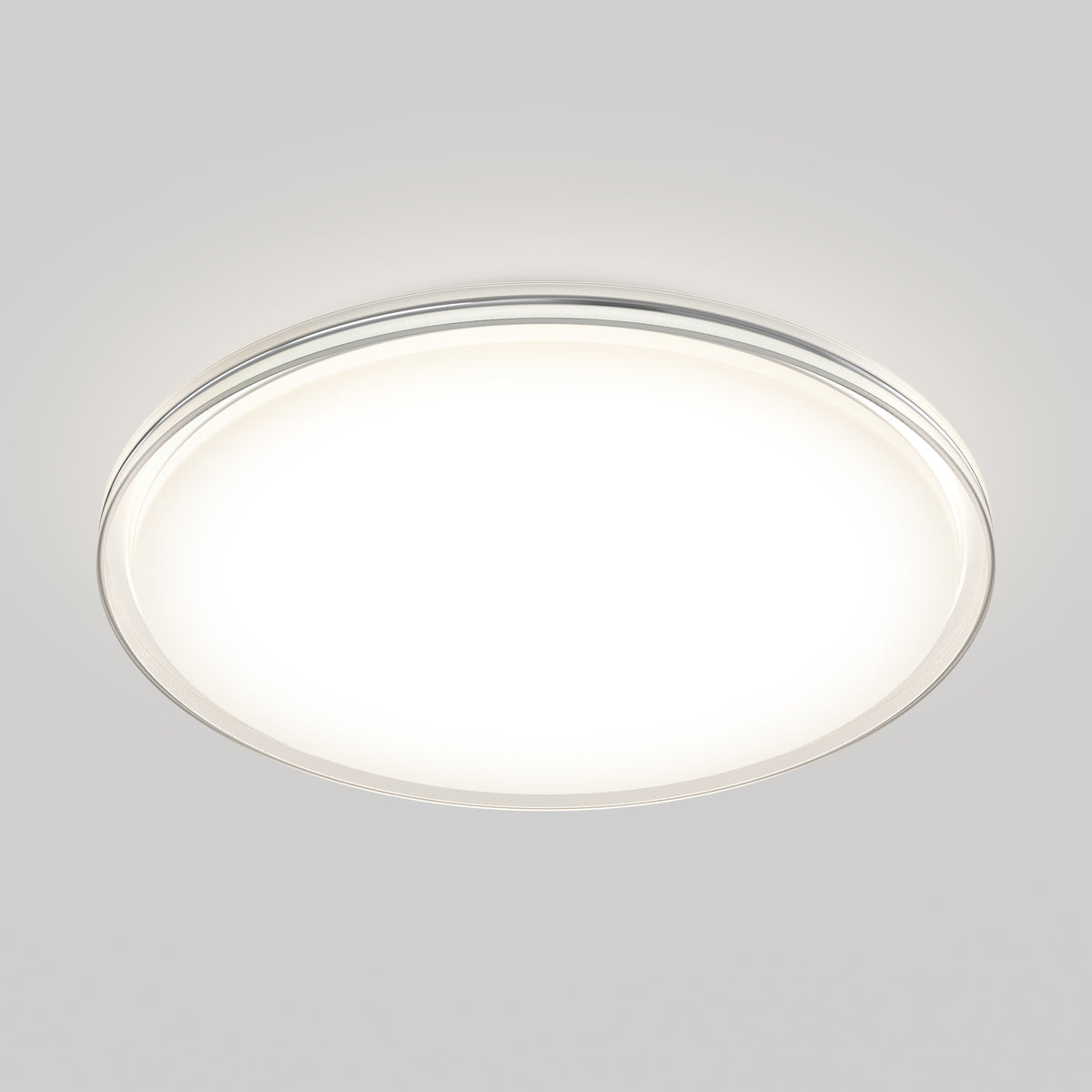 A round, flush-mounted ceiling light fixture with a white, illuminated surface and a slim metallic rim, set against a light gray background.
