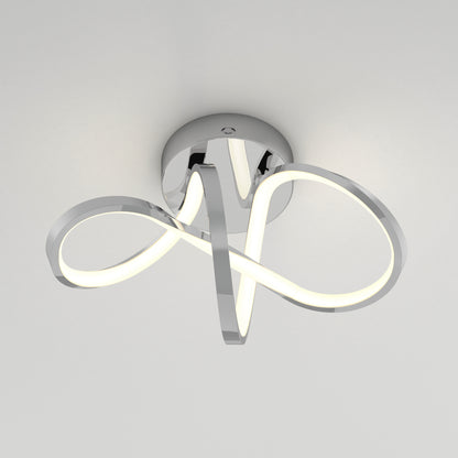 A modern, ceiling-mounted LED light fixture with sleek, chrome curved arms forming an abstract, looped design, radiating a soft white glow against a plain light-colored ceiling.