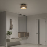 A modern, minimalist bathroom with a wall-mounted sink, folded towel, potted plant, mirror with storage cabinet, towel hanging on hooks, white door, and a round ceiling light fixture.