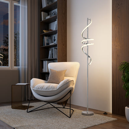 A modern living room featuring a white cushioned chair, small beige pillow, Artika’s Coda modern LED floor lamp 5CCT, a bookshelf, curtained window, and a green plant on a rug over wooden flooring.