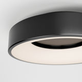 A close-up view of a modern, round black ceiling light fixture with a smooth, matte finish and a softly glowing white diffuser, mounted on a white ceiling.