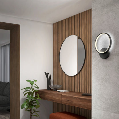 A modern entryway features a wooden console table, round mirror, potted plant, decorative items, an orange bench, and the Artika Solis modern LED indoor-outdoor wall light (5 CCT) mounted on a textured gray wall with wood paneling.