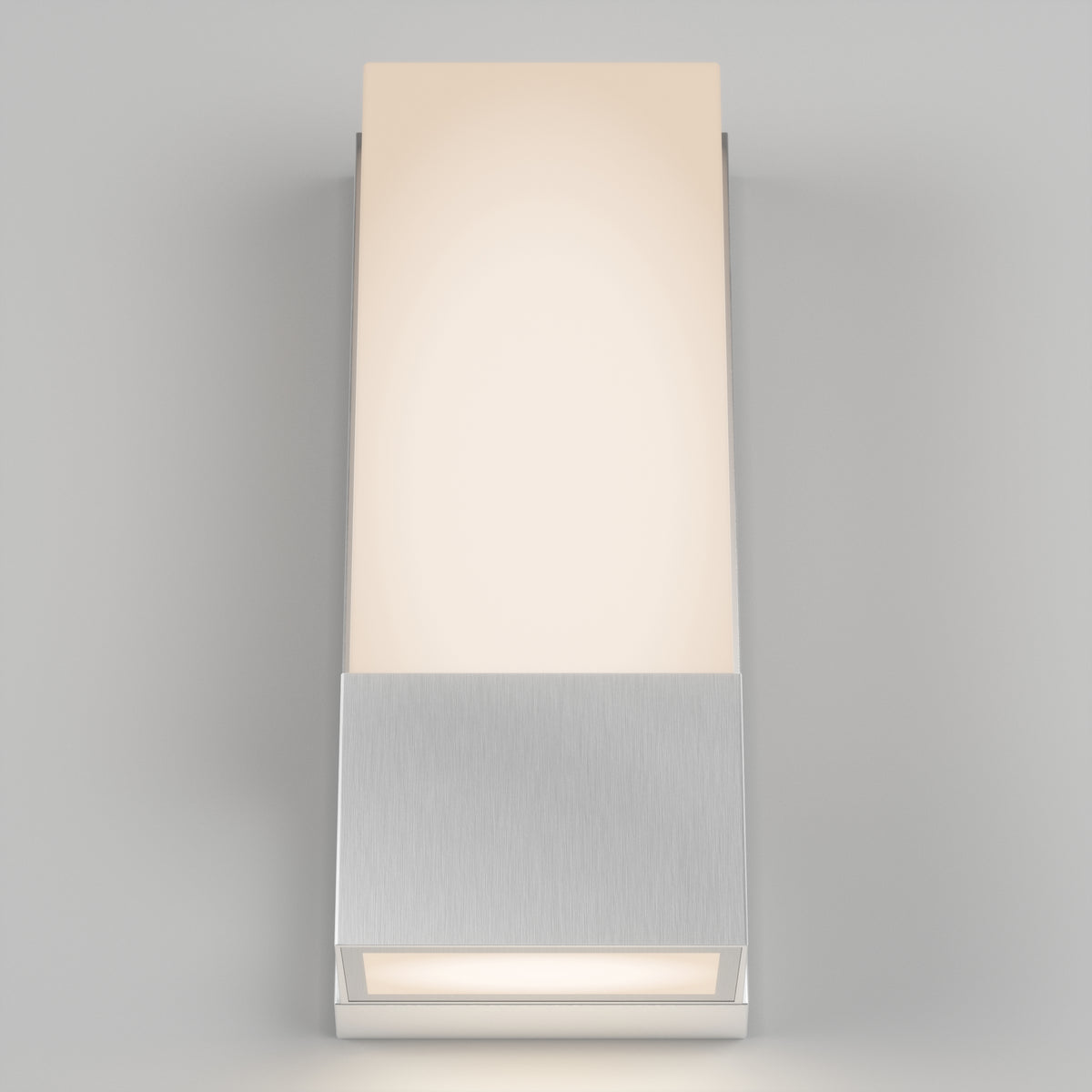 A modern wall sconce with a rectangular frosted glass shade and a brushed metal base, emitting a soft, warm light against a plain light gray wall.