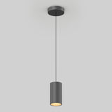 A modern black cylindrical pendant light hangs from the ceiling by a thin black cord, emitting a warm glow from the bottom against a plain light gray background.
