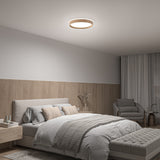 Modern bedroom with neutral tones, featuring a neatly made bed, cushioned bench, armchair with small table, wood panel accent wall, sheer curtains, and a round ceiling light.
