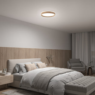 Modern bedroom featuring a large bed with neutral bedding, wooden panel accent wall, armchair, ottoman, side tables, and the Artika Callisto 15 in. LED flush mount light (5 CCT). Soft natural light streams through a window with white curtains.