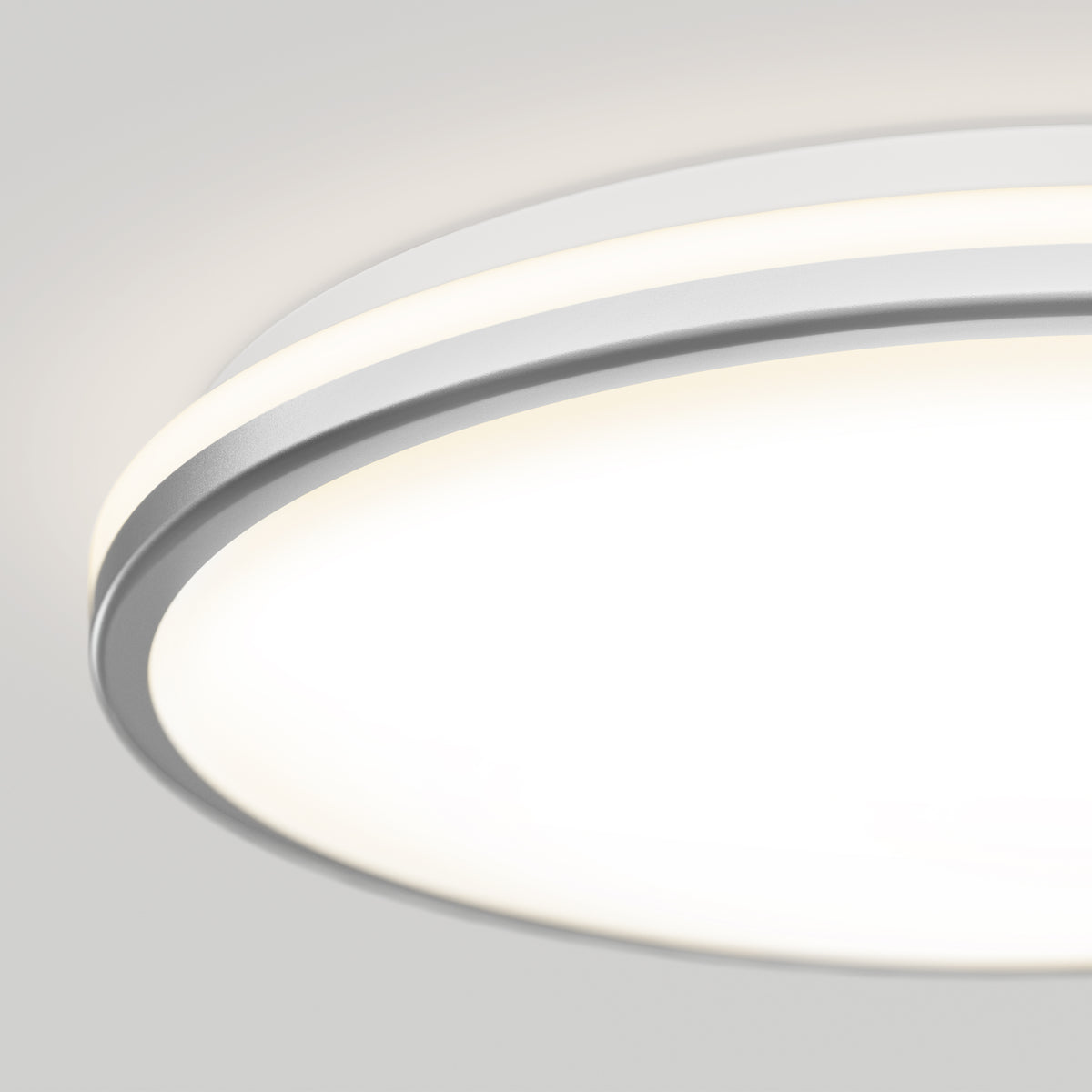 Close-up view of a modern, circular ceiling LED light fixture with a white and silver trim, glowing brightly against a plain light gray ceiling background.