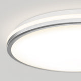 Close-up view of a modern, circular ceiling LED light fixture with a white and silver trim, glowing brightly against a plain light gray ceiling background.