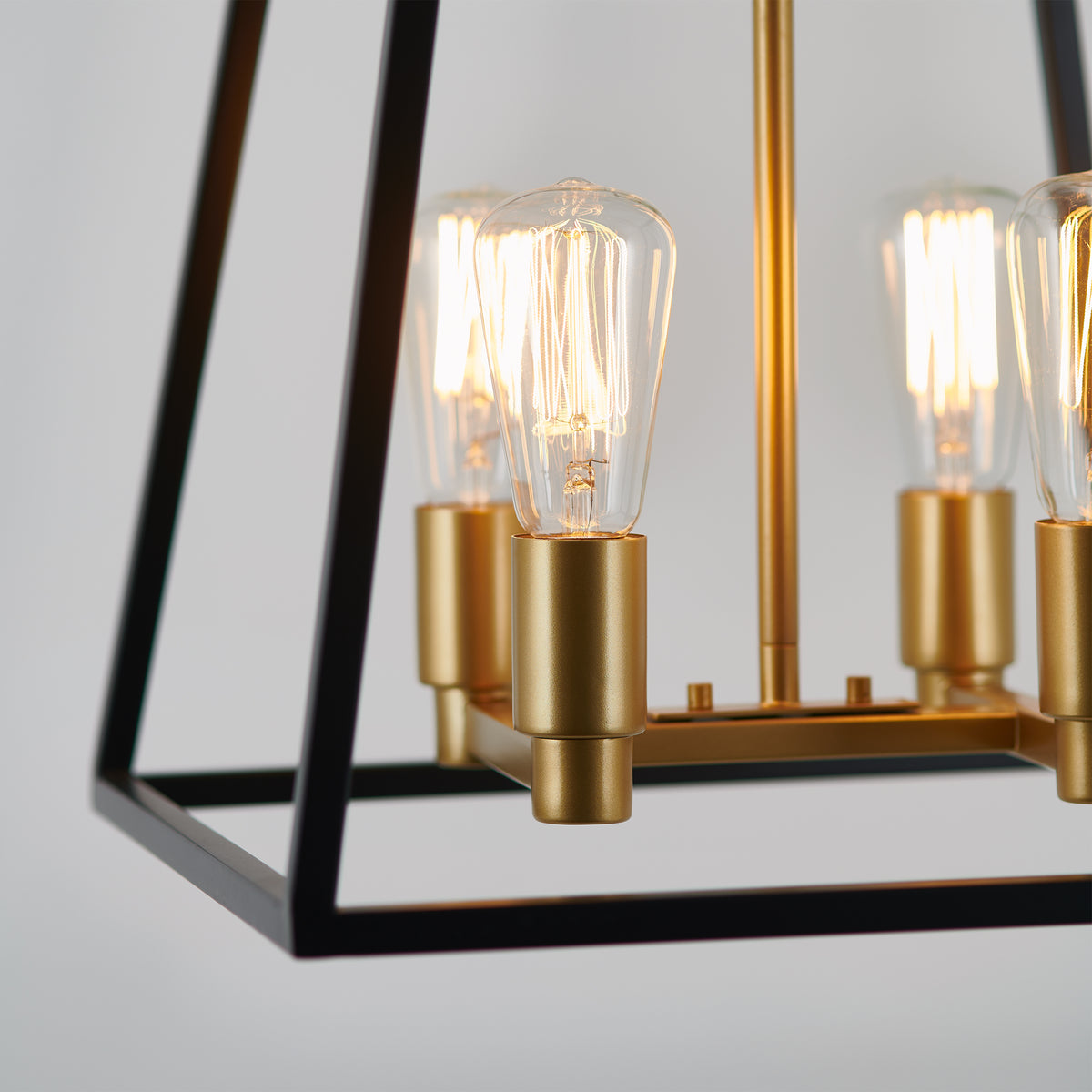 Close-up of the Artika Carter Square 4-light LED chandelier, featuring a height-adjustable black geometric frame and gold sockets. Exposed vintage-style bulbs emit a warm glow, highlighting its industrial charm.
