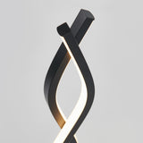 A modern table lamp with two twisting, black metal strips; one strip emits a soft white light, creating an elegant, sculptural design against a plain light gray background.
