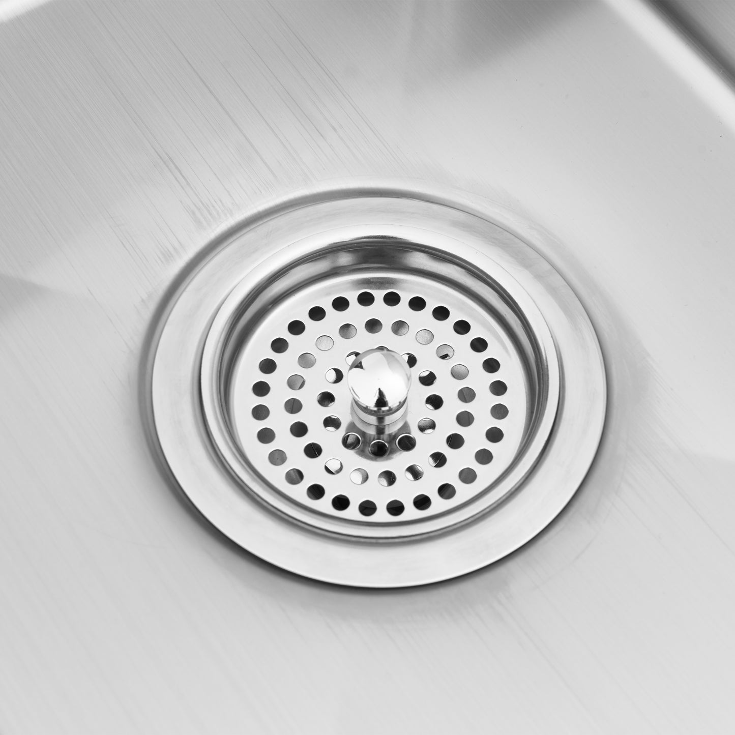 Close-up of the Artika Plaza Bar Single Bowl Sink, showcasing its clean, shiny stainless steel drain and metal strainer with round holes. The polished surface reflects light, highlighting the sinks pristine and modern appearance.