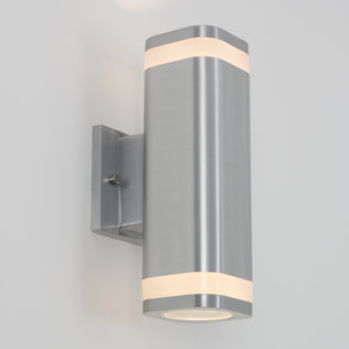 The Artika Mettle LED indoor-outdoor wall light features a modern cylindrical stainless steel design with frosted acrylic bands, mounted on a rectangular plate, and emits LED light from both ends onto a white wall.