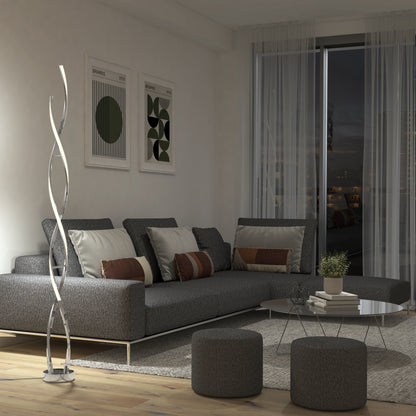Modern living room with a gray sectional sofa, patterned cushions, two round ottomans, a glass coffee table, and the Artika Swirl modern LED floor lamp. Abstract art is on the wall and large windows reveal a nighttime city view.