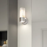 A modern wall sconce with a cylindrical marble shade and chrome base is mounted on a white wall in a contemporary interior setting.