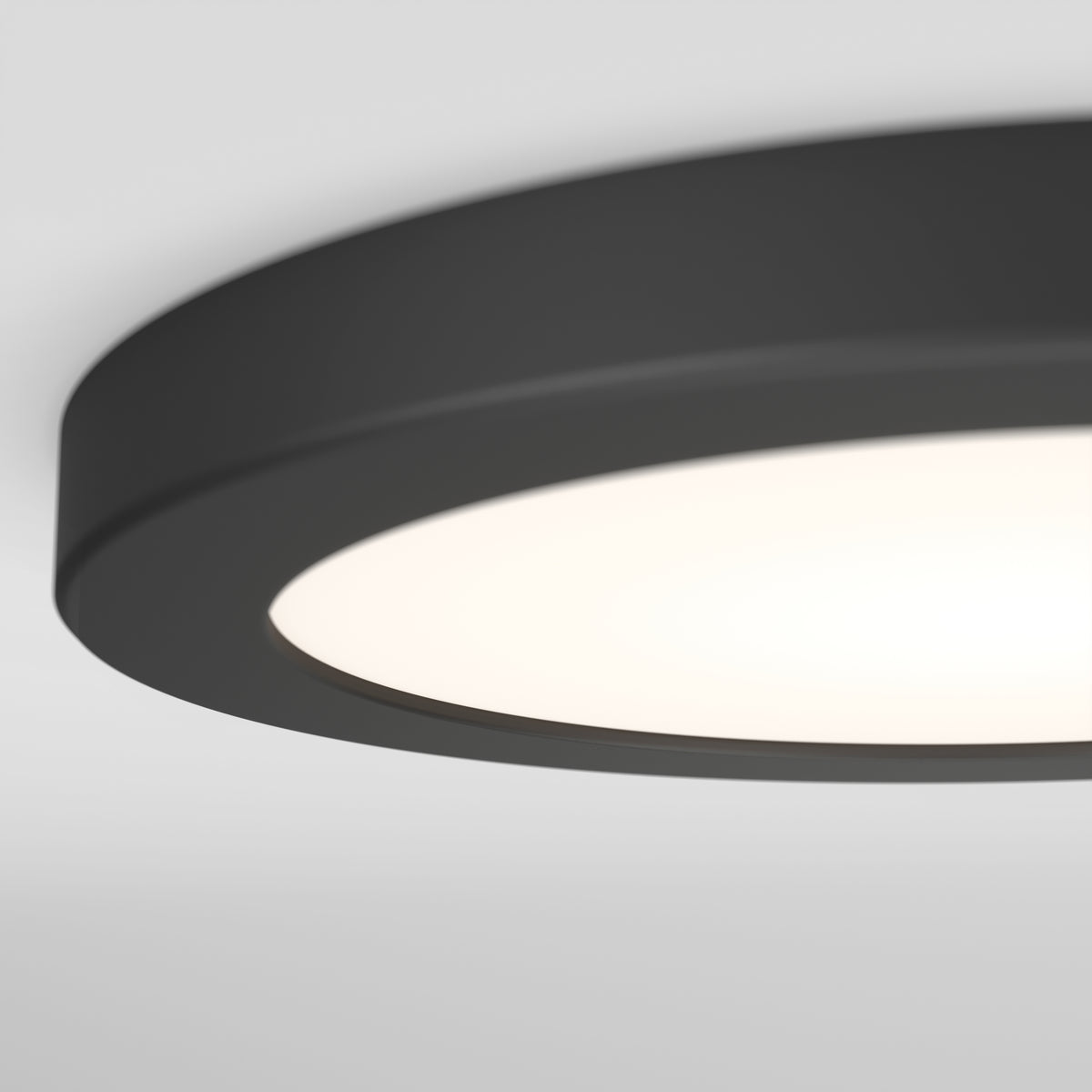 Close-up of a round, modern ceiling light fixture with a matte black rim and a white diffused surface, softly glowing against a plain white ceiling.