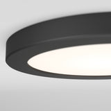 Close-up of a round, modern ceiling light fixture with a matte black rim and a white diffused surface, softly glowing against a plain white ceiling.