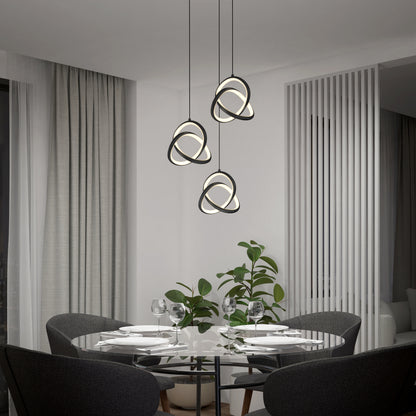 A modern dining room features a glass round table for four, gray chairs, and the Artika Zephyr 3-light LED pendant above. A leafy plant sits nearby, next to large curtains and vertical white panel dividers.