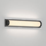 A modern wall-mounted light fixture with a long, cylindrical frosted glass shade and dark end caps, emitting a soft, even glow against a light gray wall.