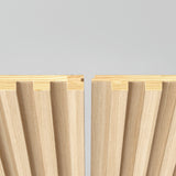 Two interlocking wooden panels with grooved, ribbed surfaces are positioned facing each other against a light gray background, showcasing their joinery design.