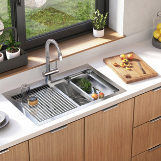 The Artika Newport twin bowl 33 in. stainless steel workstation sink features a metal drying rack with dishes, a divided basin with fresh greens, a cutting board with sliced peaches, and potted plants on the windowsill above.