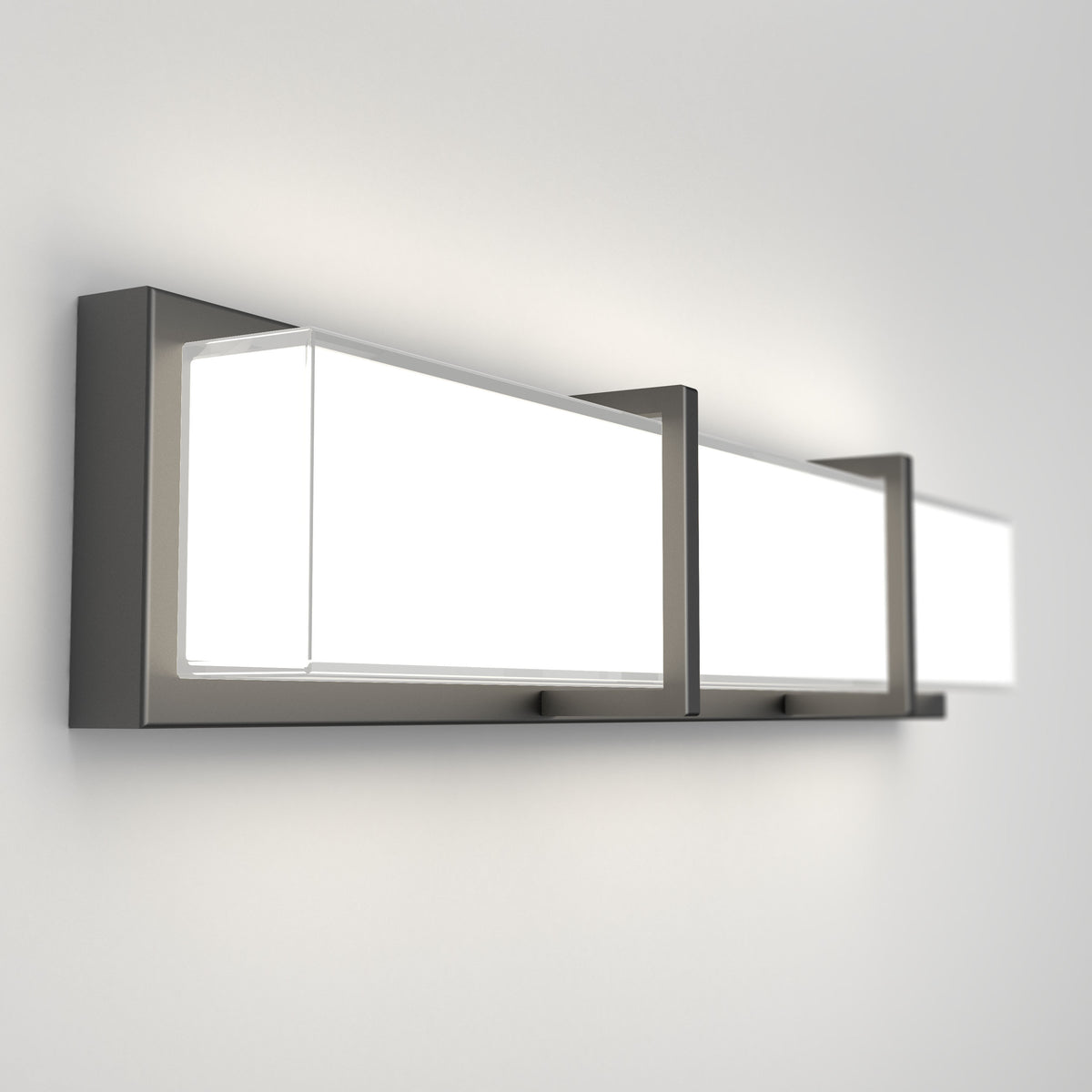 A modern rectangular wall sconce with three frosted glass panels framed in dark metal, mounted on a white wall, emitting a bright, even light.