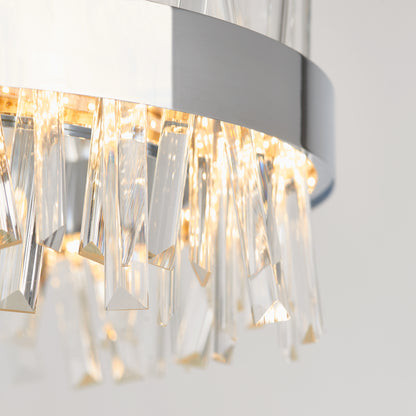 Close-up of the Artika Enchanted LED pendant light, featuring a shiny metallic frame and clear crystal prisms, glowing with warm white light against a neutral backdrop.