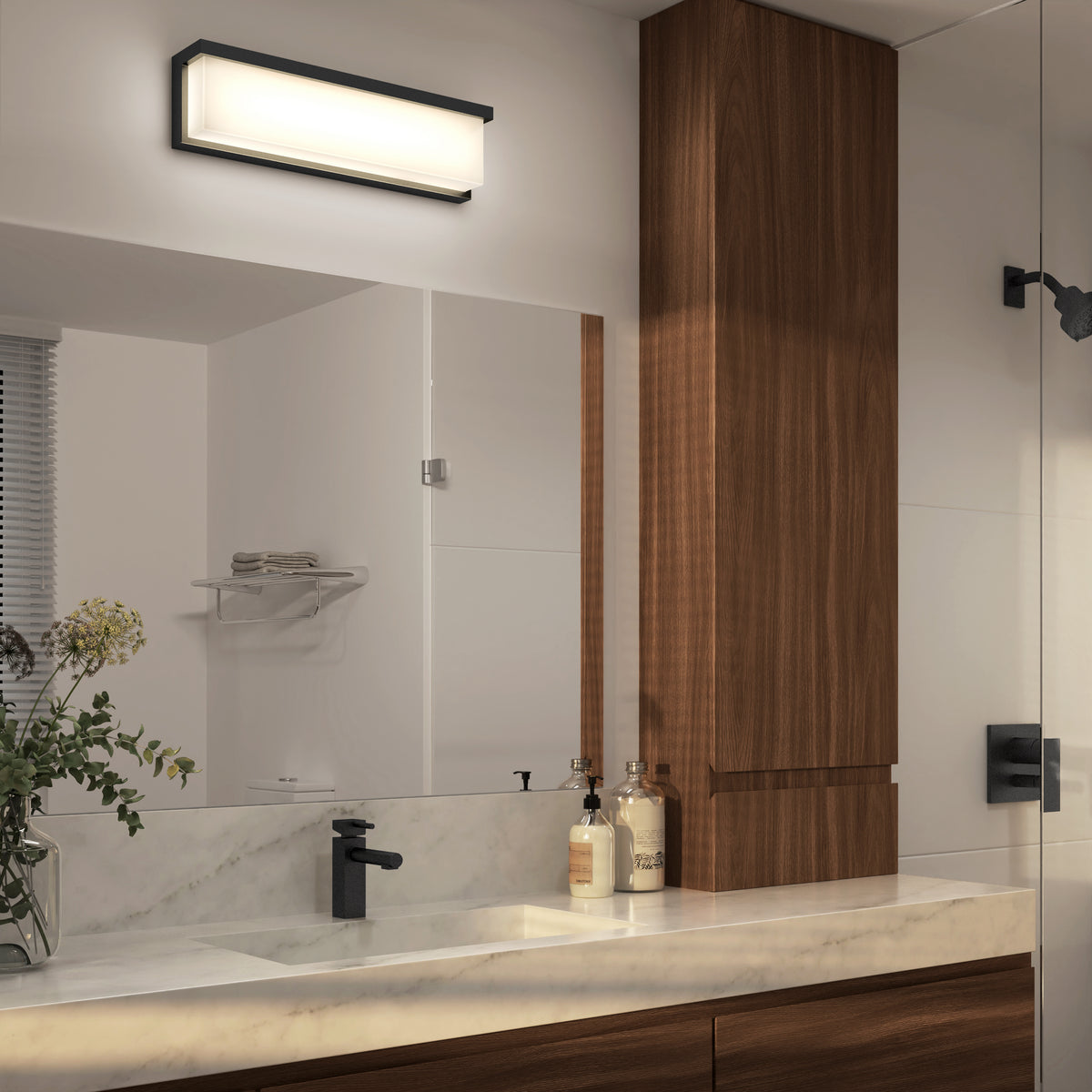 Modern bathroom with a marble countertop, wooden cabinets, black faucet, soap dispensers, a vase with greenery, large mirror, and a rectangular wall-mounted light fixture above the mirror.